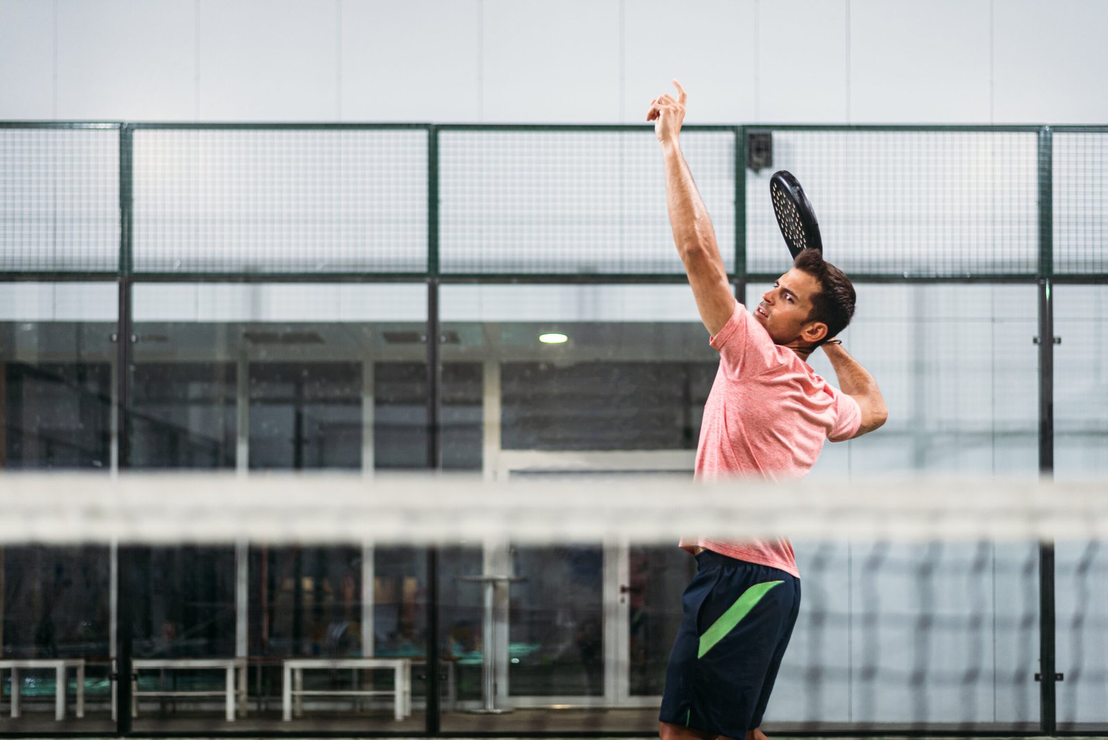 Man playing padel in a green grass padel court indoor behind the net